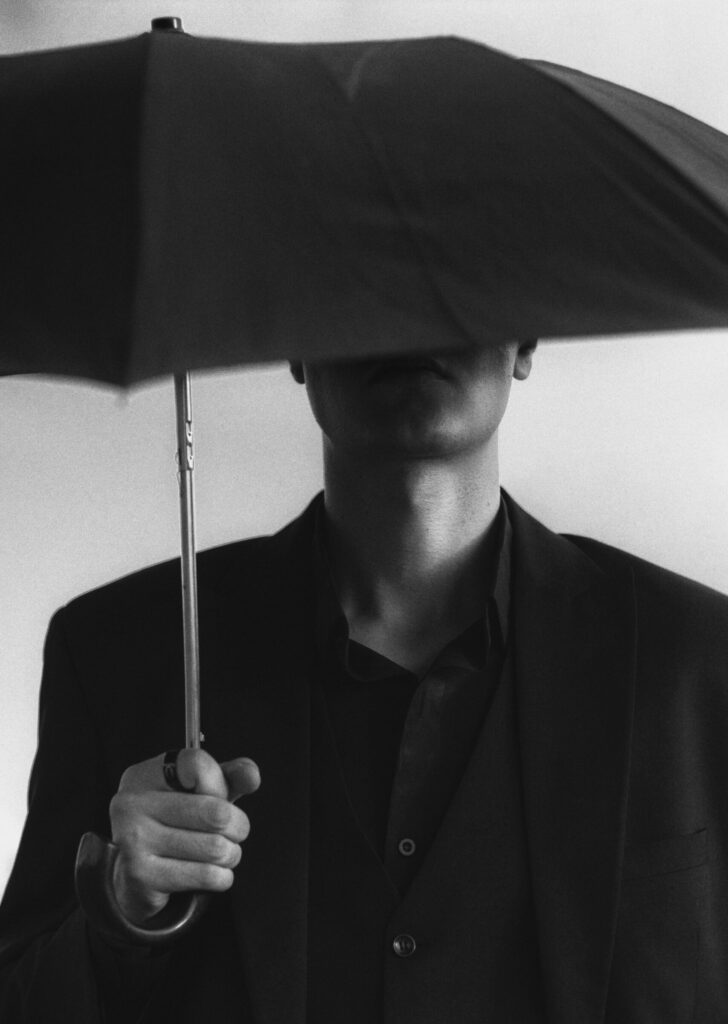 Elegant black and white image of a man in a suit holding an umbrella, evoking mystery and sophistication.