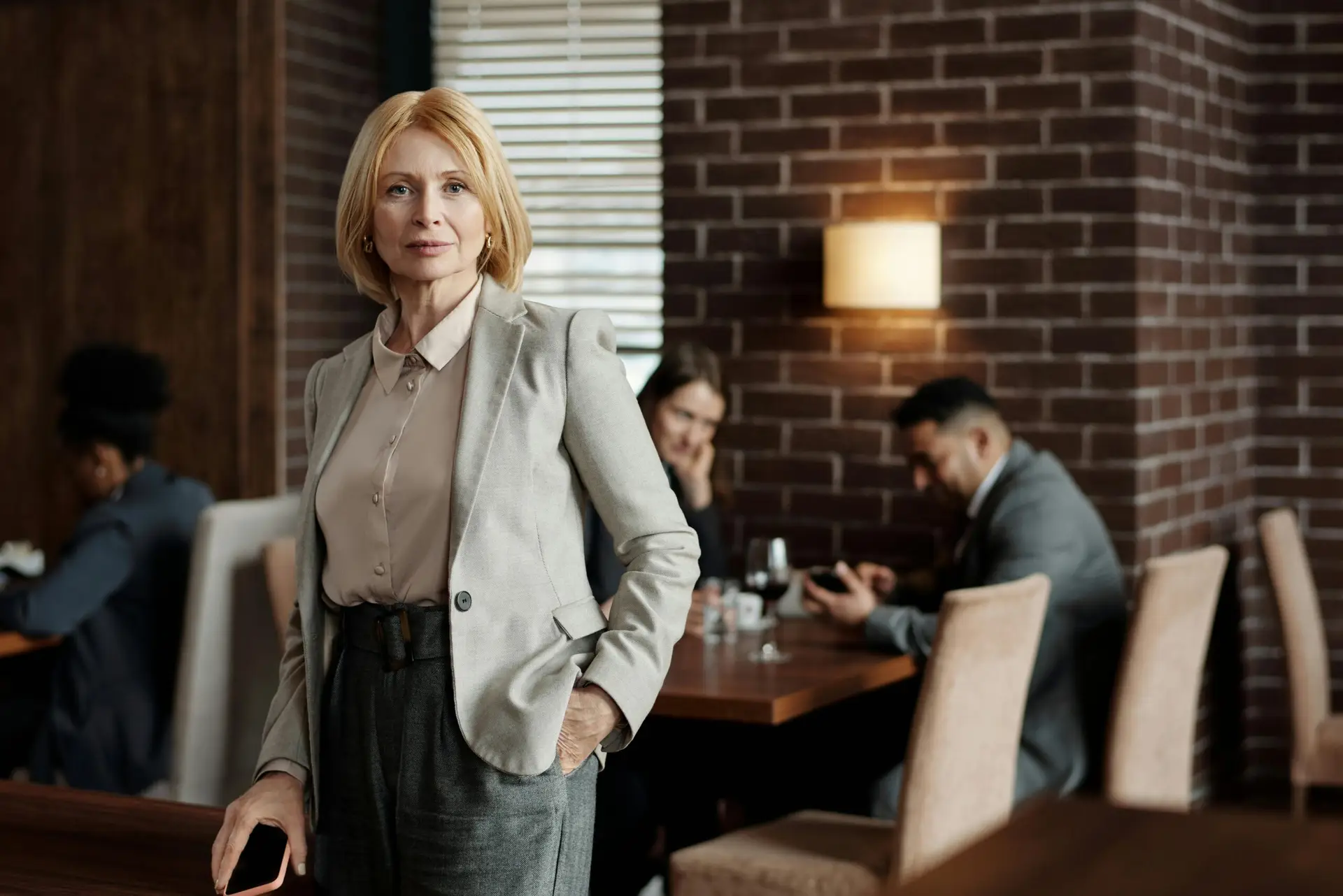 Mature businesswoman in gray blazer standing confidently in a stylish café interior.