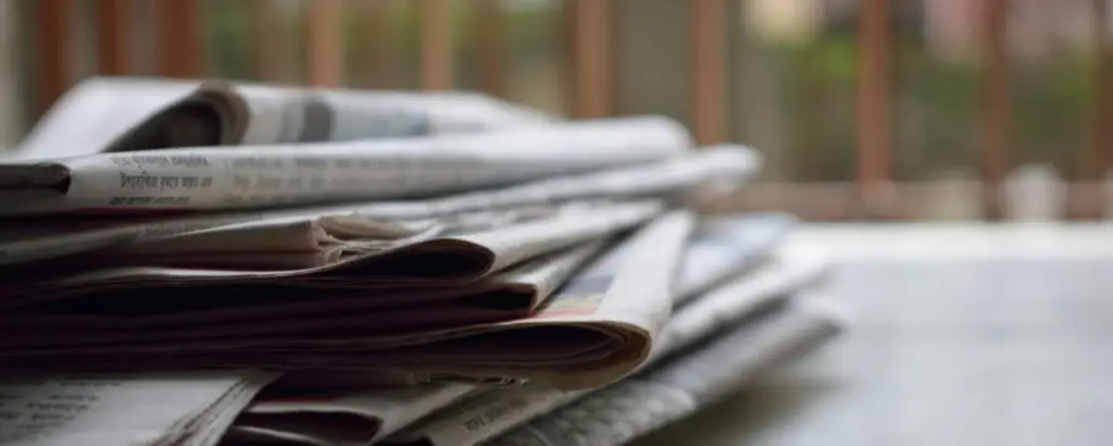 A close-up of a stack of newspapers resting on a desk, symbolizing information and media.
