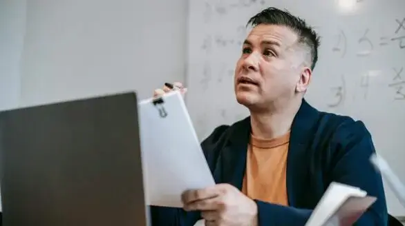 Educator discussing concepts during an online session, sitting at a desk with a laptop.