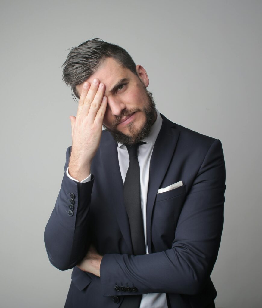 A portrait of a stressed businessman in a dark suit and tie, holding his head thoughtfully.